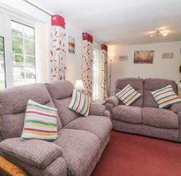 A living room with two fabric sofas with striped cushions next to windows with patterned curtains at Sycamores Rosecraddoc Lodge near Liskeard