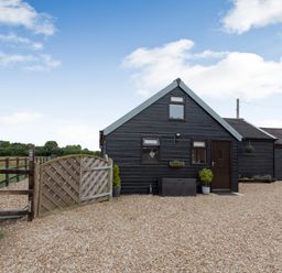 A black wooden single-story building with a gravel driveway and wooden gate at The Nook in Louth