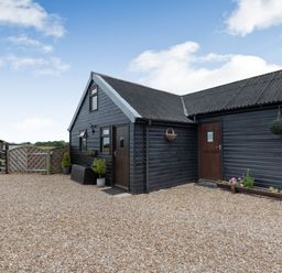 A black wooden building with two doors and windows surrounded by gravel and plants at The Nook in Louth