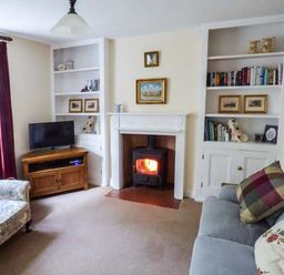 A living room with a fireplace a television on a wooden stand and bookshelves at Woodside Cottage in Brompton-by-Sawdon