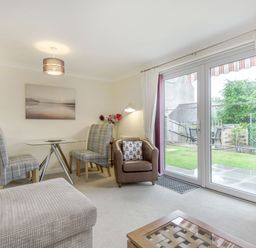 A living room with a glass table and chairs a leather armchair and large windows overlooking a garden at Kymin View in Monmouth