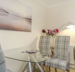 A glass dining table with three checkered chairs a vase of flowers and a wall lamp at Kymin View in Monmouth