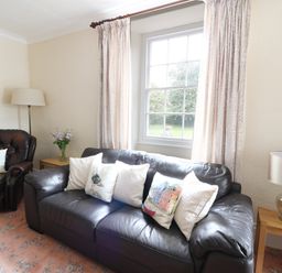 A living room with a black leather sofa and armchair with cushions beside a window at Dolau Farmhouse in Lampeter