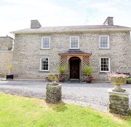 Exterior view of a stone farmhouse with a wooden porch and gravel driveway at Dolau Farmhouse in Lampeter