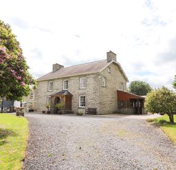 A stone farmhouse with a gravel driveway and trees nearby at Dolau Farmhouse in Lampeter
