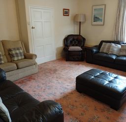 A living room with sofas armchair ottoman floor lamp and window at Dolau Farmhouse in Lampeter