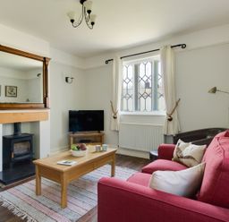 A living room with a red sofa a wooden coffee table a fireplace a television and a window with white curtains at The Old School House in Piddletrenthide