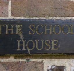 A wooden sign with the words The School House on a brick wall at The Old School House in Piddletrenthide