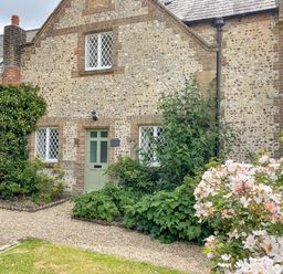 Front view of a stone and brick house with a green door surrounded by plants and flowers at The Old School House in Piddletrenthide