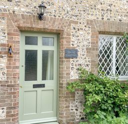An exterior wall with a green door next to a window with lattice panes and a plaque that says The Old School House in Piddletrenthide
