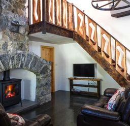 A living room with a stone fireplace wooden staircase leather sofas and a television at The Well House in Kinvara County Galway