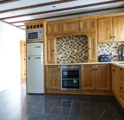 A kitchen with wooden cabinets tiled backsplash oven refrigerator microwave toaster and wine rack at The Well House in Kinvara County Galway