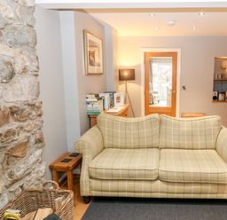 A living room with a checkered sofa stone wall and wooden floor at Haddef in Nefyn