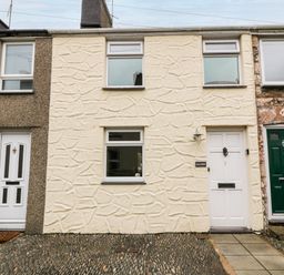 The front of a cream stone textured terraced house with white door and three windows at Haddef in Nefyn