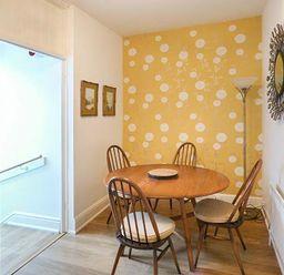 A dining area with a round wooden table and four wooden chairs against a yellow patterned accent wall at High Ridge in Ambleside