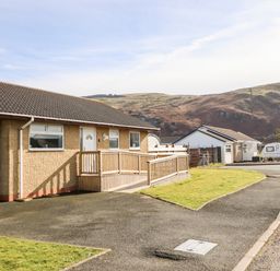 A single story house with a ramp and a driveway near a road with hills in the background at Sealyons in Fairbourne near Dolgellau