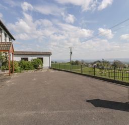A paved driveway next to a white house with plants and a metal fence overlooking a green field at Moors Farm in Littledean