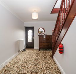 A hallway with floral carpet a wooden staircase a chest of drawers and a round mirror at Moors Farm in Littledean