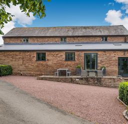 A stone building with multiple black windows and doors a gravel driveway and some outdoor seating at Teal Barn Annexe in St Weonards
