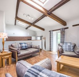 A sitting room with leather sofas wooden furniture exposed ceiling beams and skylights at Teal Barn Annexe in St Weonards