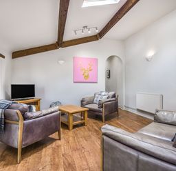 A sitting room with leather armchairs a wooden coffee table a TV on a wooden stand and a pink artwork on the wall at Teal Barn Annexe in St Weonards