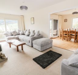 A living room with a gray sectional sofa a wooden coffee table a fireplace and an adjacent dining area with a wooden table and chairs at Middle Hivron in Bleddfa