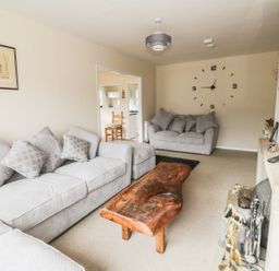 A living room with grey sofas a wooden coffee table a wall clock and a fireplace at Middle Hivron in Bleddfa
