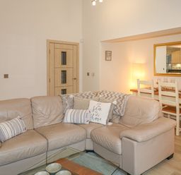A living room with a beige leather sofa and a dining table with chairs and a mirror on the wall at The Creekside in Looe