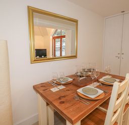 A dining table set with plates wine glasses and candles next to a mirror and two chairs at The Creekside in Looe