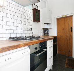 A kitchen with a wooden countertop gas stove oven dishwasher white tiled wall and wooden door at 13 Castle Hill in Lostwithiel