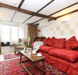 A living room with a red sofa, a wooden coffee table, a striped armchair, and framed pictures on the wall at 13 Castle Hill in Lostwithiel