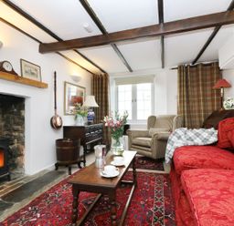 A living room with a red sofa, armchair, wooden coffee table, fireplace, and patterned rug at 13 Castle Hill in Lostwithiel