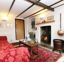 A living room with a red sofa a wooden coffee table flowers on table a fireplace and wooden door at 13 Castle Hill in Lostwithiel