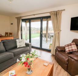 A living room with a sofa armchair coffee table and dining table near glass doors showing a patio at Caban Nant Ddu in Rhayader