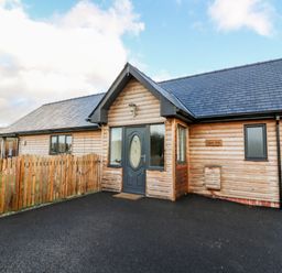 A wooden cabin with a gray door and a fenced yard at Caban Nant Ddu in Rhayader