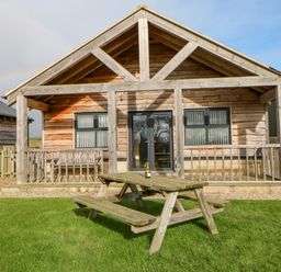 A wooden cabin with a covered porch and a picnic table on grass at Wansbeck in Longframlington near Alnwick
