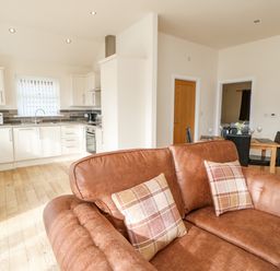 An open plan room with a brown sofa, a kitchen with white cabinets and a dining table with black chairs at Wansbeck in Longframlington near Alnwick