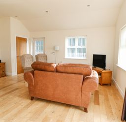 A living room with a brown sofa two armchairs a wooden TV stand with a television and wooden flooring at Wansbeck in Longframlington near Alnwick