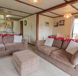 A living room with two brown sofas and a matching ottoman adjacent to an open kitchen and dining area at Roe Deer Lodge in Castlewigg near Whithorn