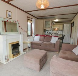 A living room with two sofas a fireplace and a kitchen area at Roe Deer Lodge in Castlewigg near Whithorn