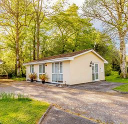 A single-story house with windows and doors surrounded by trees and grass at Brook Cottage Rosecraddoc Lodge near Liskeard