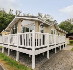 A beige cabin with large windows and a white railing around a raised deck next to a paved driveway at 95 The Haven in Wisemans Bridge near Saundersfoot