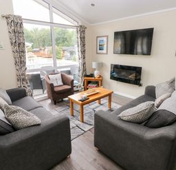 A living room with two sofas, an armchair, a coffee table, a wall-mounted TV and fireplace at 95 The Haven in Wisemans Bridge near Saundersfoot