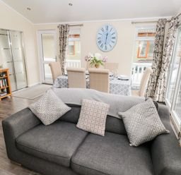 A living room with a dark grey sofa and dining table with six chairs and a clock on the wall at 95 The Haven in Wisemans Bridge near Saundersfoot