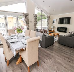 An open plan living room and dining area with a table set for six and sofas facing a wall-mounted TV at 95 The Haven Wisemans Bridge near Saundersfoot