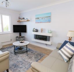 A living room with a sofa coffee table wall mounted tv and fireplace at Captains Retreat in Christchurch