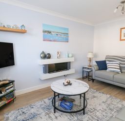 A living room with grey sofas a round coffee table a wall-mounted fireplace and a TV stand at Captains Retreat in Christchurch