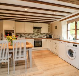 A kitchen with wooden table and chairs appliances and window at Owls Nest in South Molton