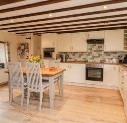 A kitchen with wooden beams a dining table with chairs and flowers on the table at Owls Nest in South Molton