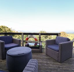 An outdoor deck with wicker chairs cushions a round table and a view of trees and hills at Snowdon View in Harlech